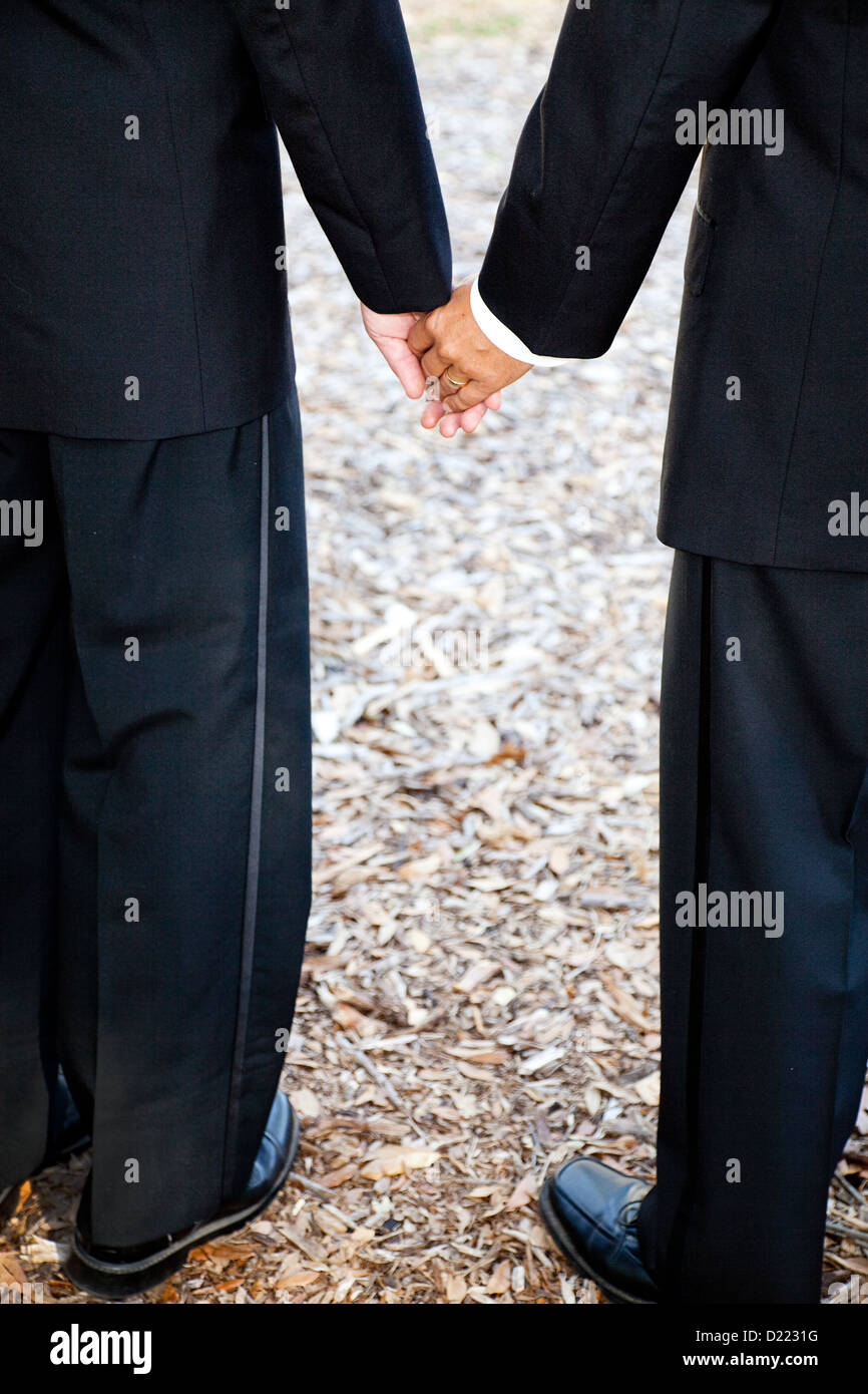 Closeup view of interracial gay couple getting married in tuxedos and holding hands. Wedding band is visible.  Stock Photo
