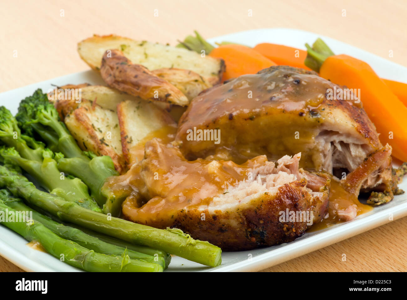 Dinner of roasted belly pork with asparagus, broccoli, carrots and potato wedges - studio shot Stock Photo