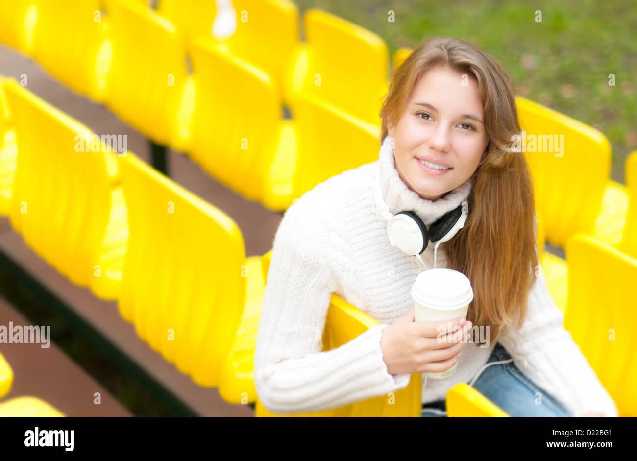 Beautiful happy student relaxing outdoor. Pretty smiling girl having break with coffee and book on her knees sitting in row of y Stock Photo