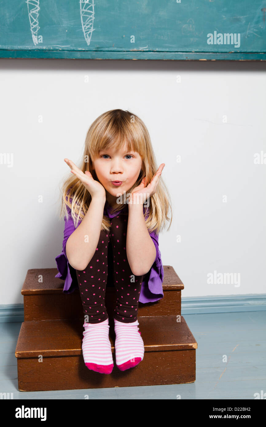 Studio portrait of young girl sitting in front of chalkboard in classroom blowing kiss Stock Photo