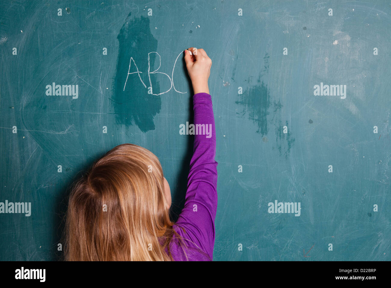 Young girl writing letters of the alphabet on chalkboard with chalk Stock Photo
