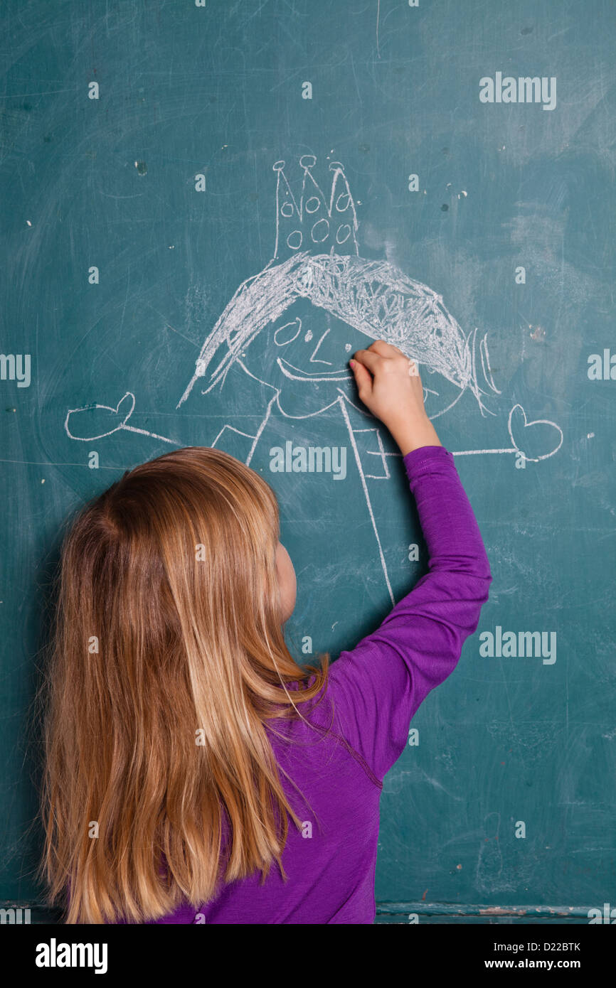 Young girl drawing an image of a princess with crown on chalkboard Stock Photo