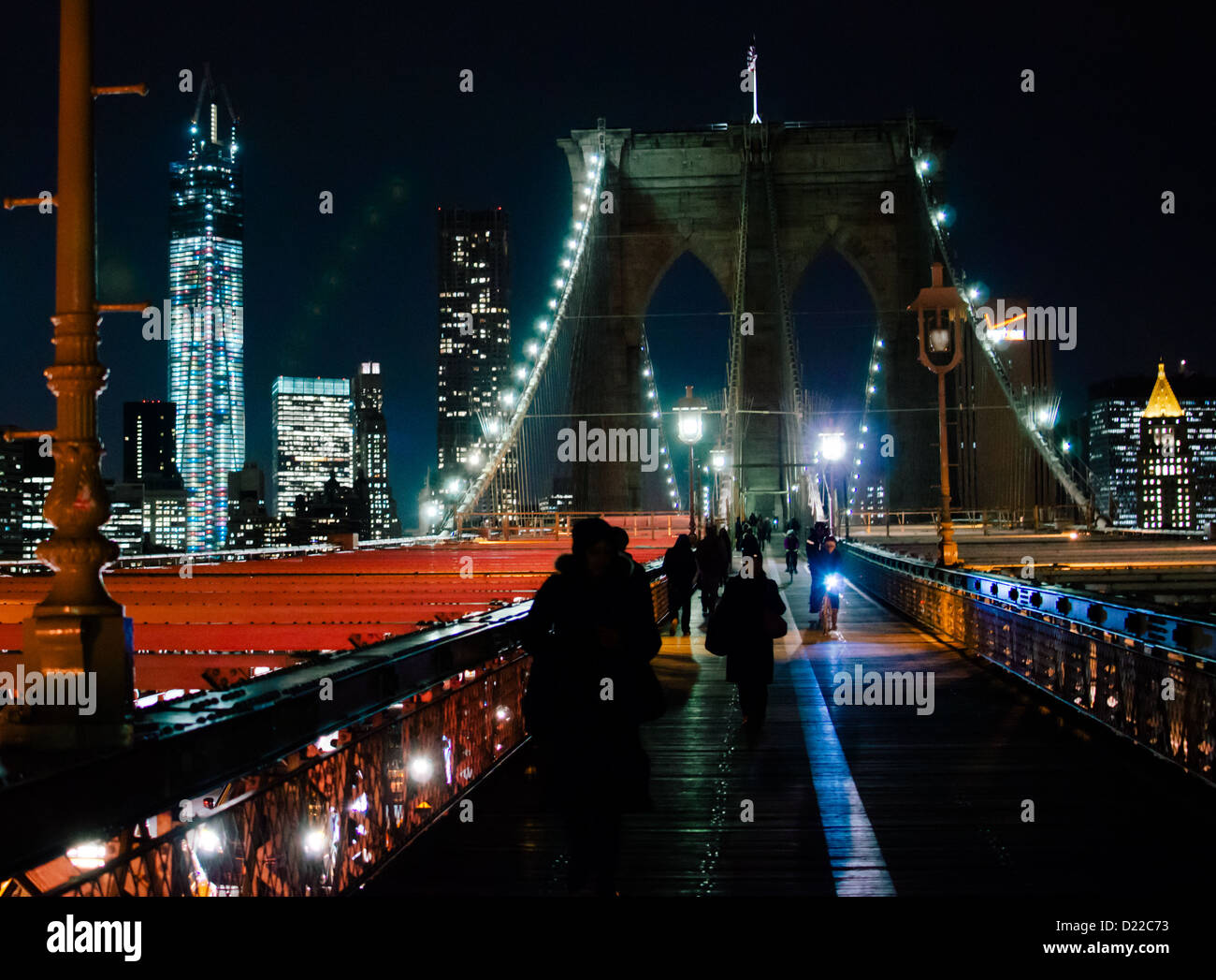 Brooklyn Bridge with Manhattan behind it, lit up at night with pedestrians walking and cycling over. Stock Photo