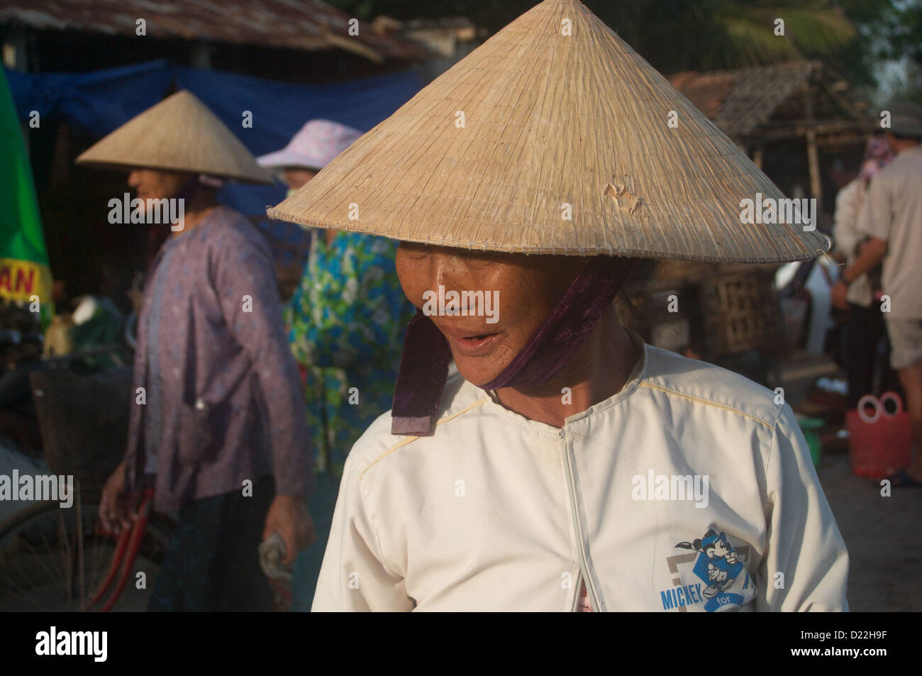 An elderly Vietnamese lady in the typical conical hat walks along the harbor of the Duy Hai Fishing Village, Hoi An, Vietnam Stock Photo
