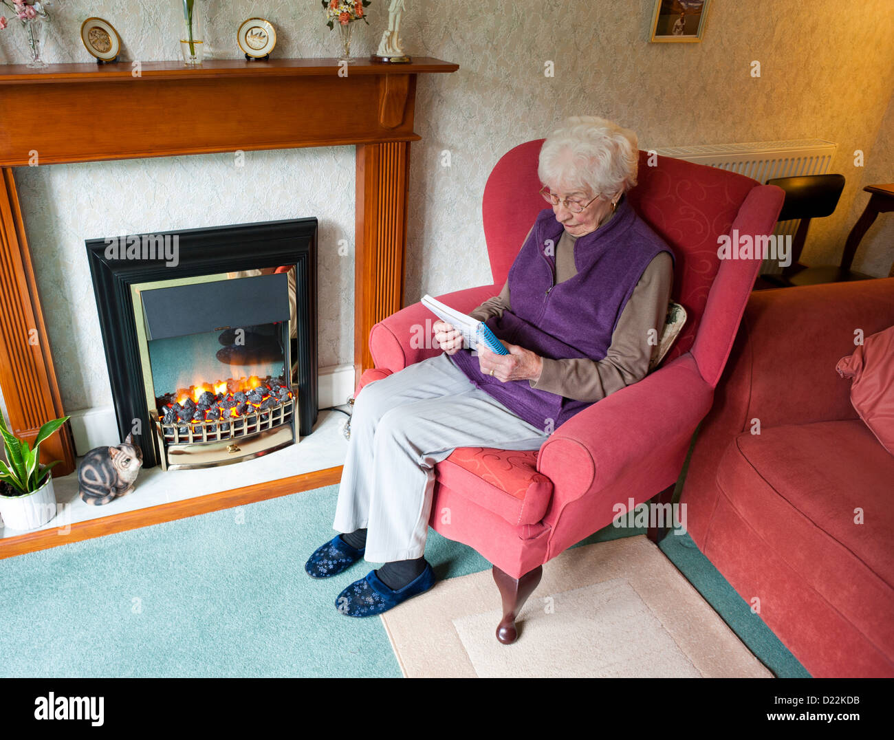 An old woman sitting by an electric fire doing a crossword Stock Photo