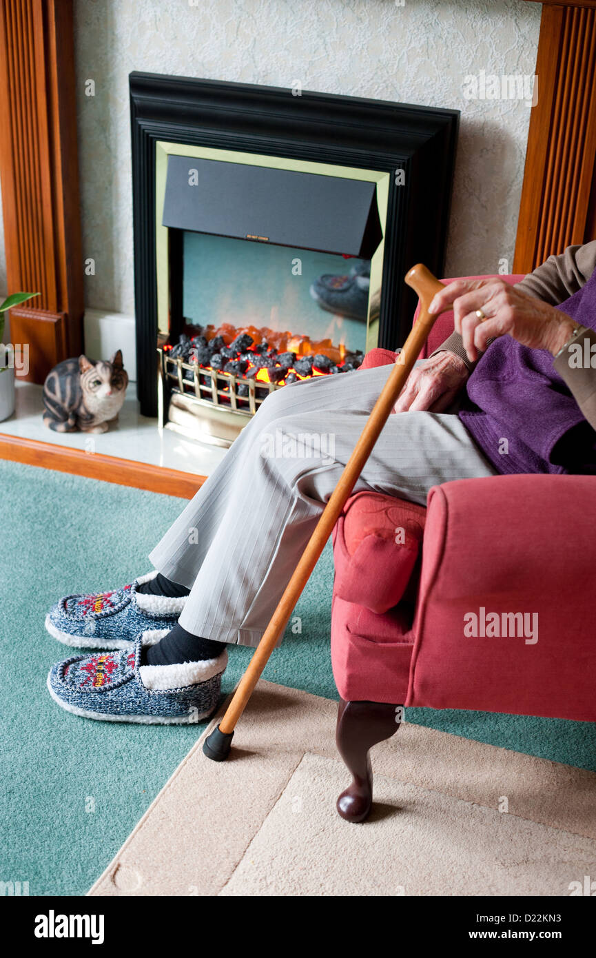 An elderly woman sitting by an electric fire. Stock Photo