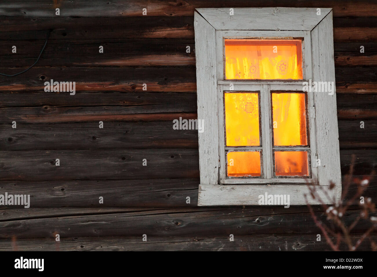 bright yellow lighting window of rural log house in winter Stock Photo