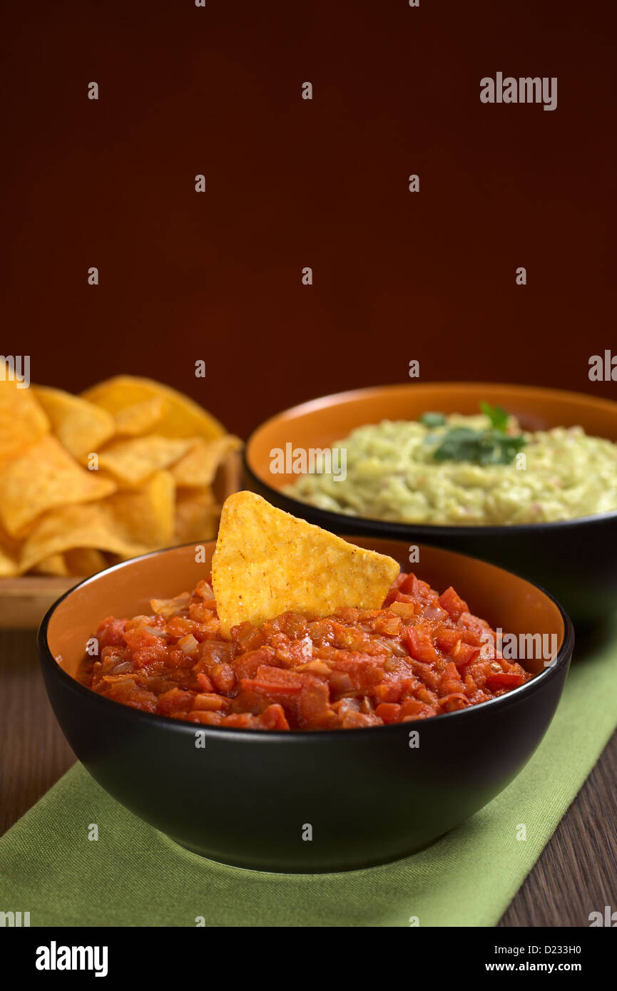 Tomato salsa with a nacho in it and guacamole sauce in the back