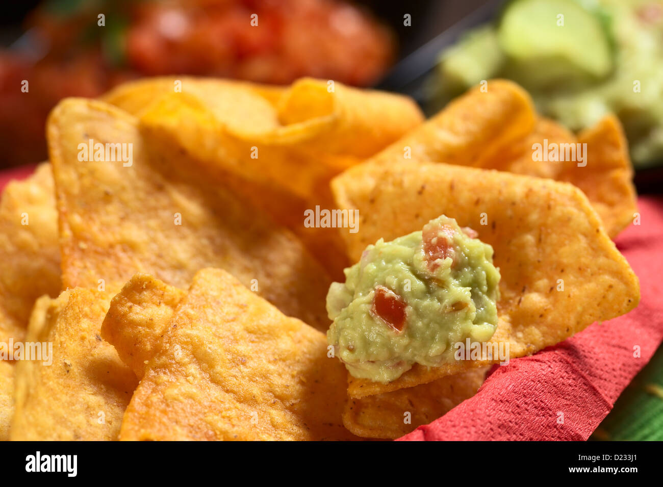 Fresh homemade guacamole (a Mexican sauce made of avocado cream, tomato and onions) on a nacho in a bowl full of nachos Stock Photo