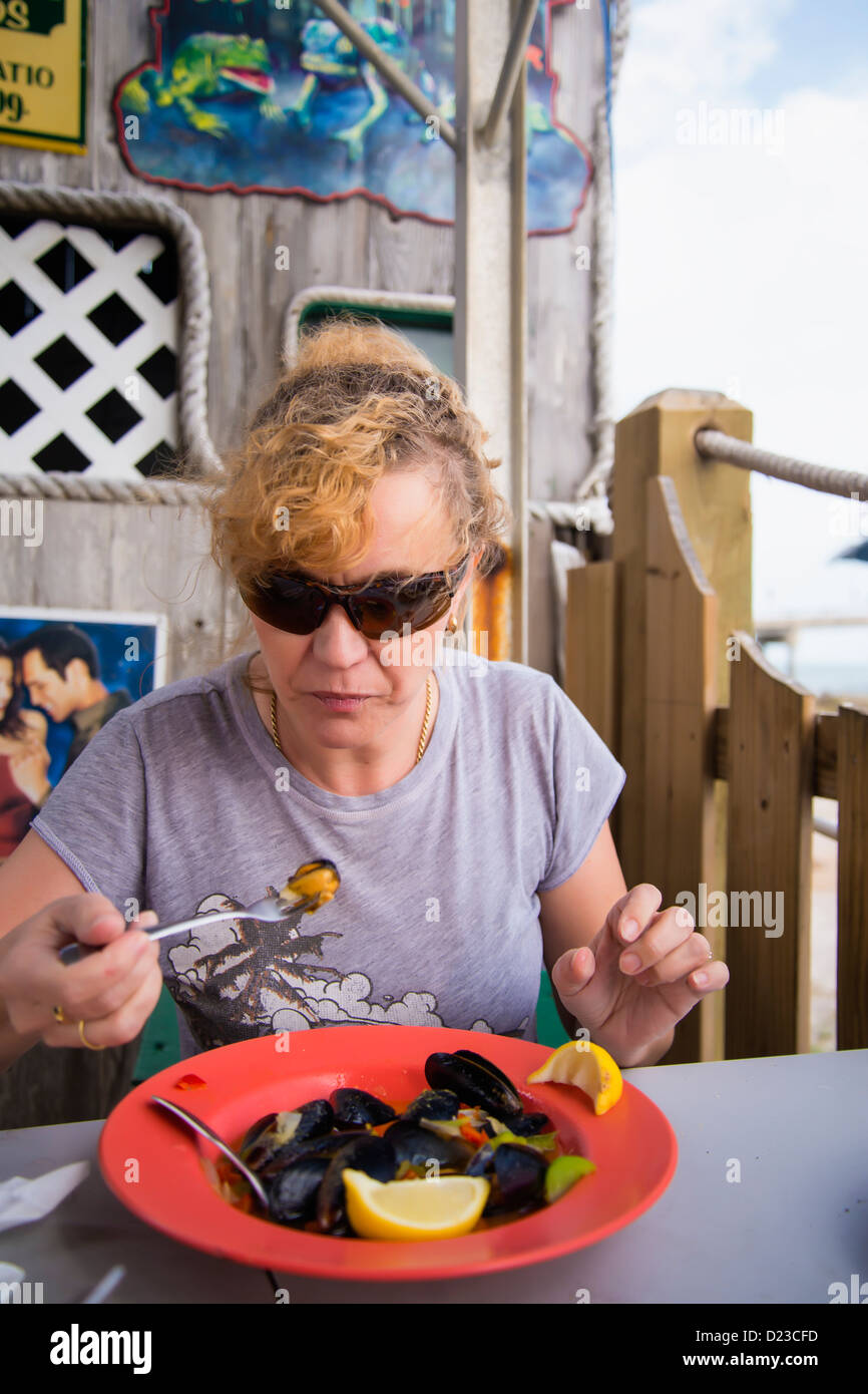 Woman, 45, Caucasian, enjoying mussels dish in beach bar restaurant