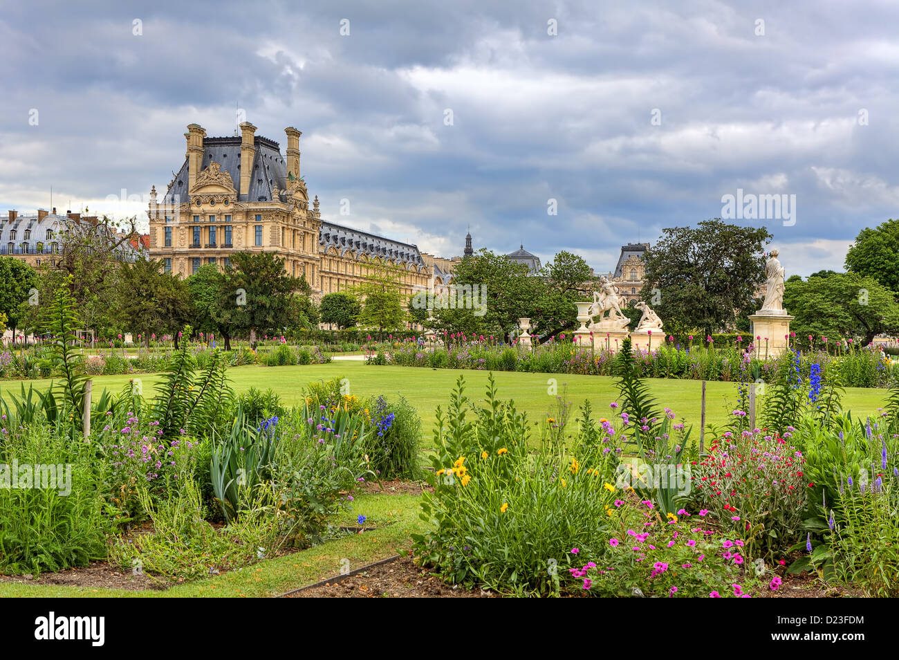 Green lawn, statues and flowers at famous Tuileries Garden and Louvre museum on background under cloudy sky in Paris, France. Stock Photo