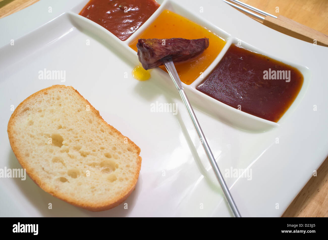 Place setting, Fondue plate with different sauces, bread and meat skewer Stock Photo