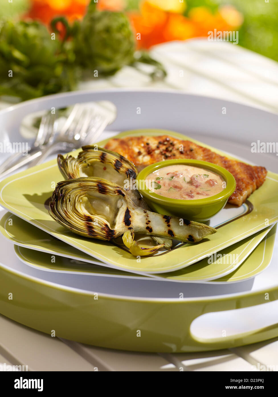Grilled artichokes served with fish and a dipping sauce in an outdoor