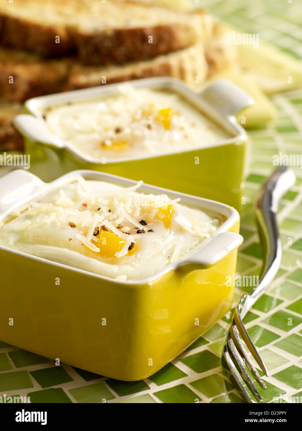 Baked eggs topped with parmesan in small baking dishes served with toast Stock Photo