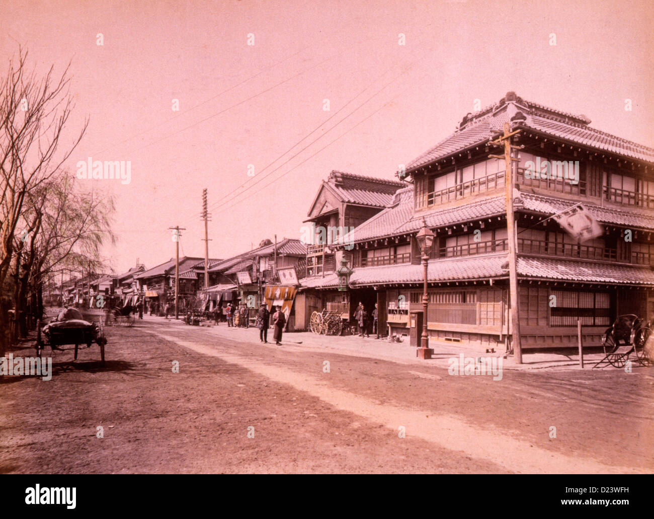 Street  scene in town with commercial and/or residential buildings along one side, and street lamps and utility poles; a couple, at center, standing in the middle of the street. Yokohama, Japan, circa 1890 Stock Photo