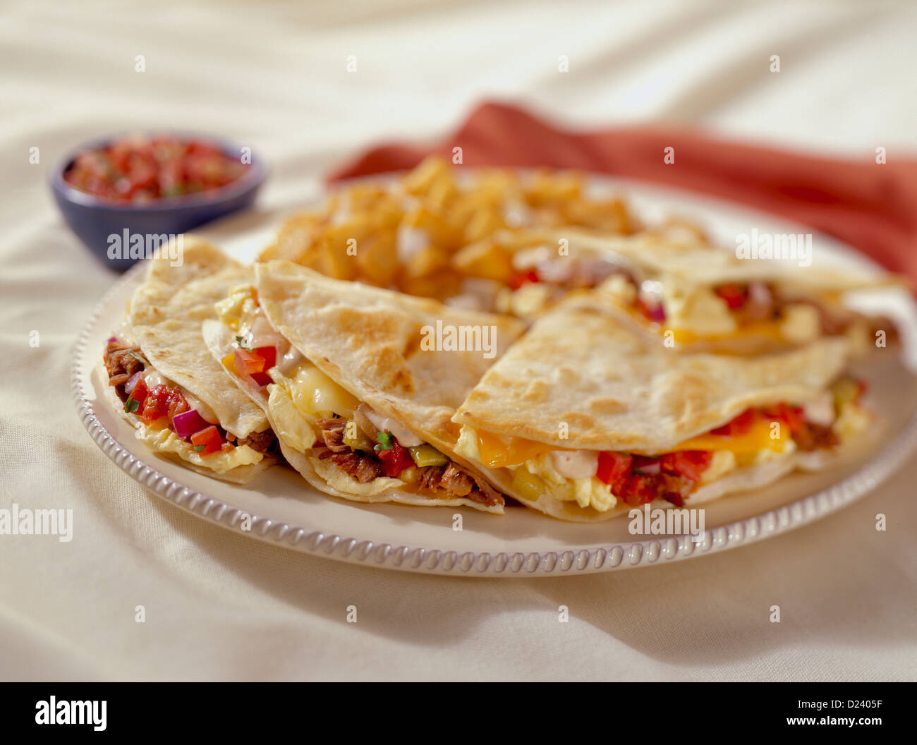 A breakfast quesadilla stuffed with eggs, bacon, tomatoes and melted cheese served with potatoes and salsa Stock Photo