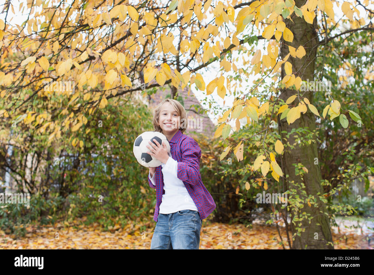 Germany, Leipzig, Boy playing football under autume tree Stock Photo