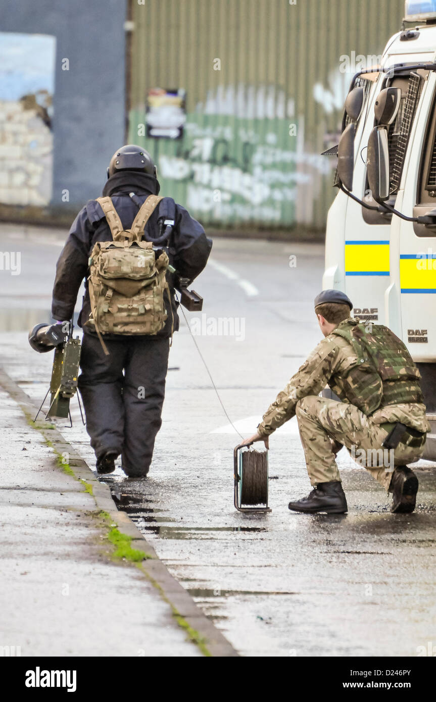 Belfast, Northern Ireland, UK. 14th January 2013.   Army ATO from 321 Squadron, 11 EOD Regiment, dressed in a bomb-proof suit walks towards a suspect device carrying Electronic Counter Measure (L) and a controlled explosion 'pig stick' (R). His colleague holds a cable reel for the detonation cord. Stock Photo