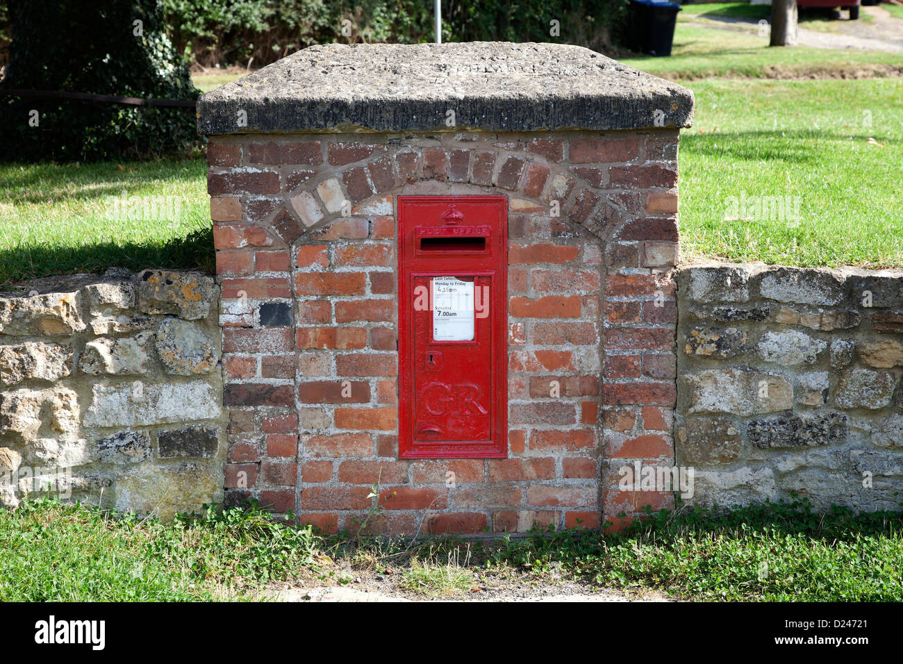 Red post box set into wall on village green Stock Photo