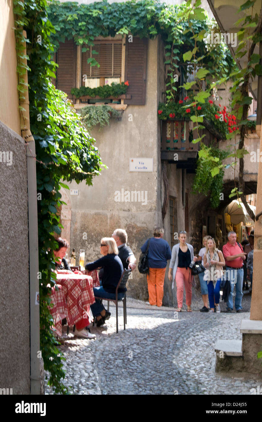 Visitors enjoying light refreshments in a small square, Via Casella, in the medieval town of Malcesine on the eastern shore of Lake Garda in the Venet Stock Photo
