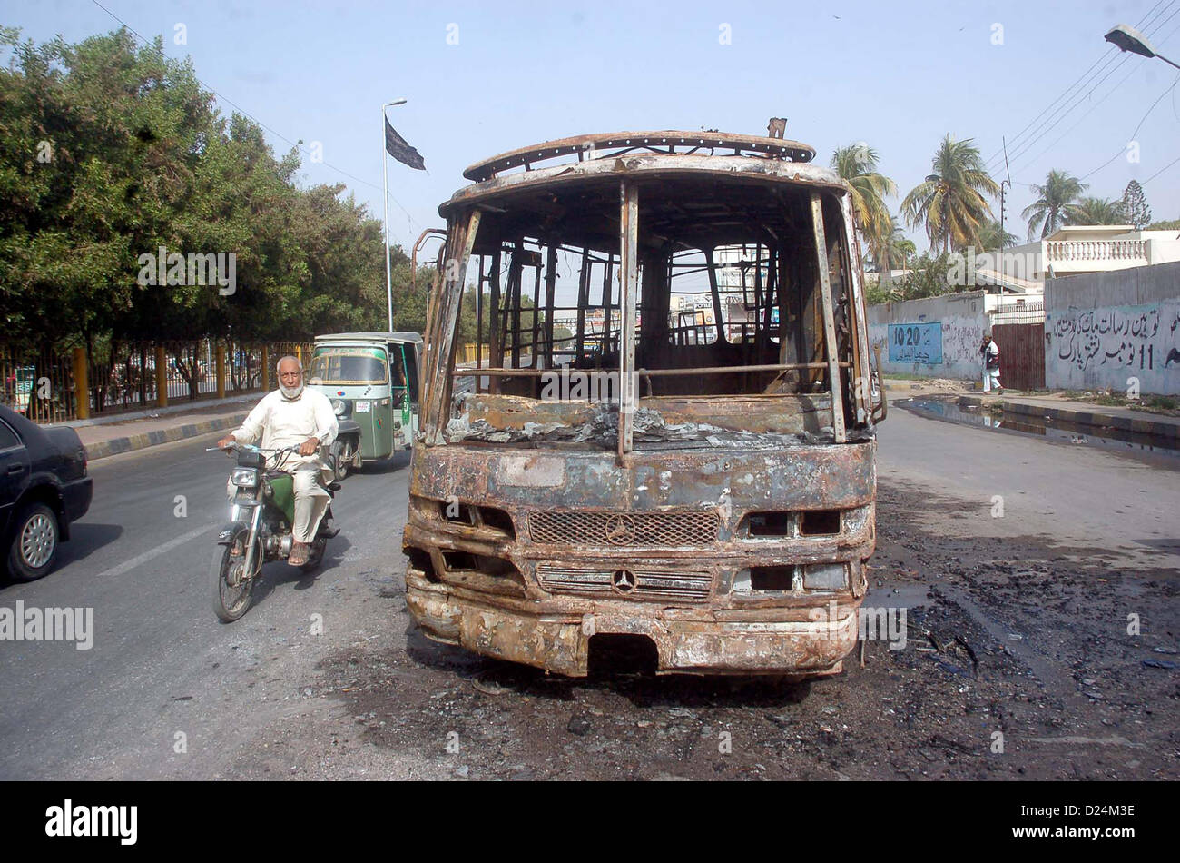 Commuters pass through burnt bus that was torched by  unidentified persons during protest against killing and genocides of Shiite Muslims across the  Pakistan, at New M.A Jinnah Road in Karachi on Monday, January 14, 2013. Stock Photo