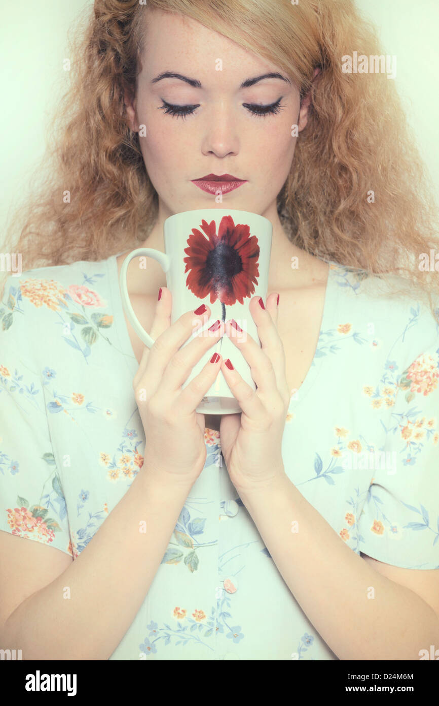 a woman in a floral dress is drinking out of a mug Stock Photo