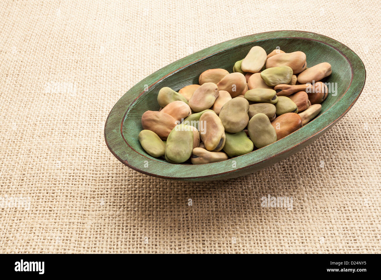 fava (broad) beans in a rustic wood bowl against burlap canvas Stock Photo