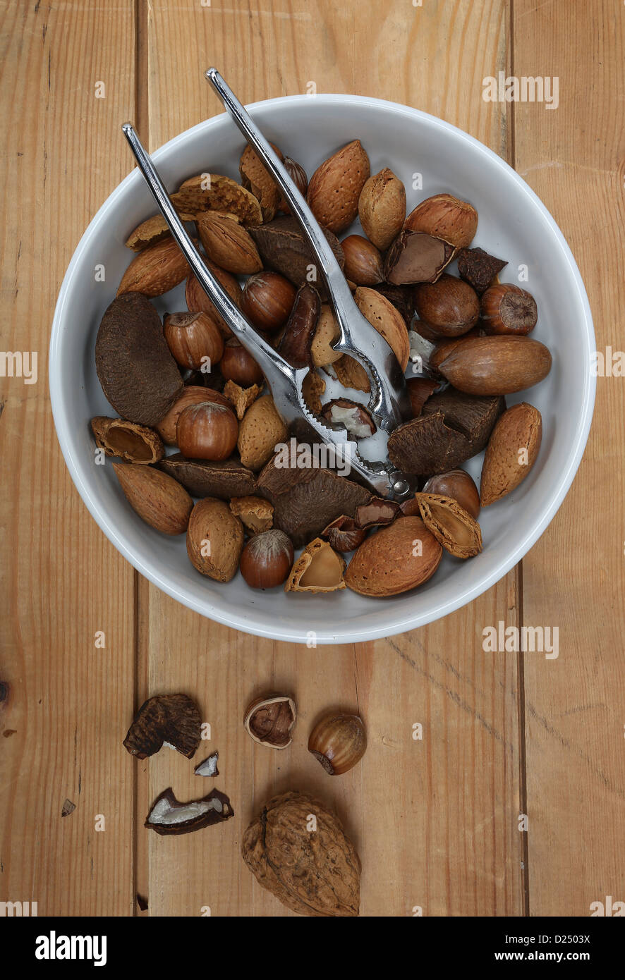 mixed nuts in a white bowl with a metal nut cracker, photographed on old wood Stock Photo