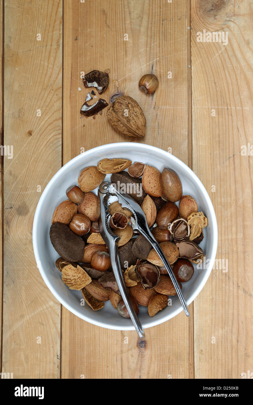mixed nuts in a white bowl with a metal nut cracker, photographed on old wood Stock Photo