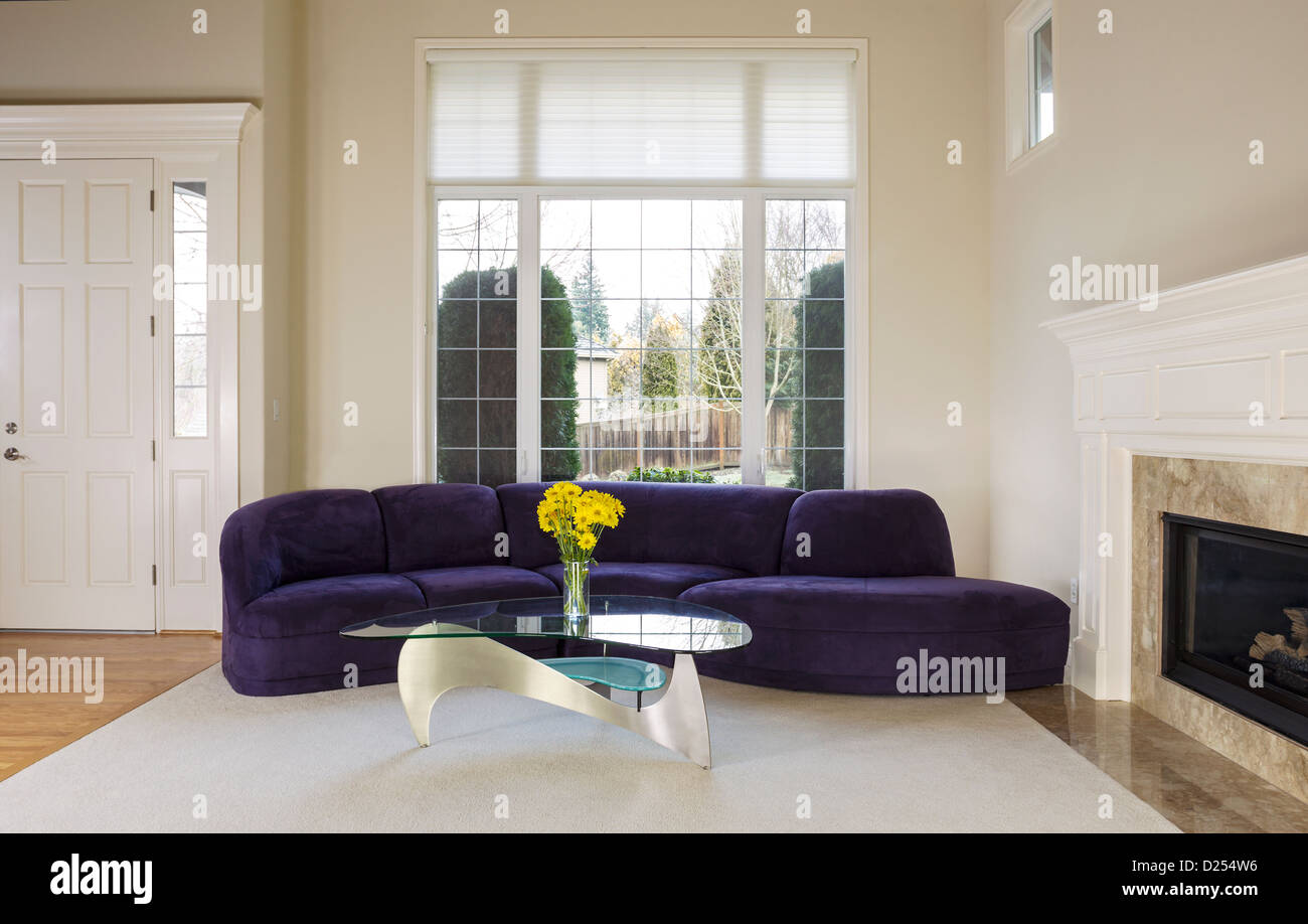 Large family living room with suede sofa, glass table in front of large double pane window with daylight coming in to room Stock Photo