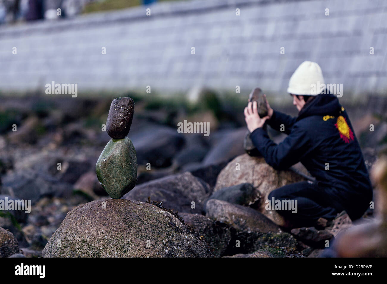young man wearing a white toque or hat,  on the rocky beach of English Bay, Vancouver British Columbia Canada, stacking stone Stock Photo