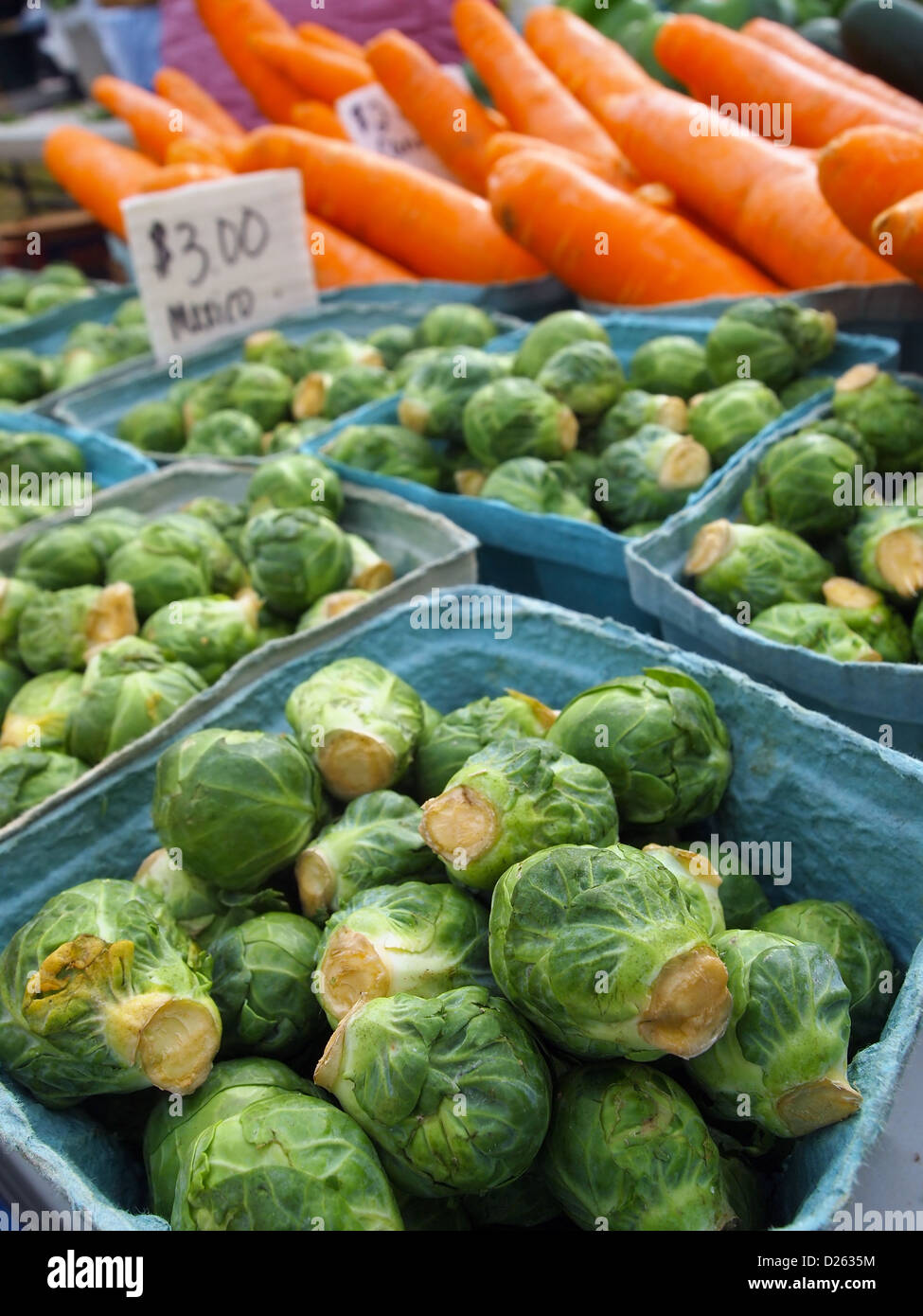 Fresh, green, organic brussels sprout for sale at a local farmer's markets, with carrots in the background. Stock Photo