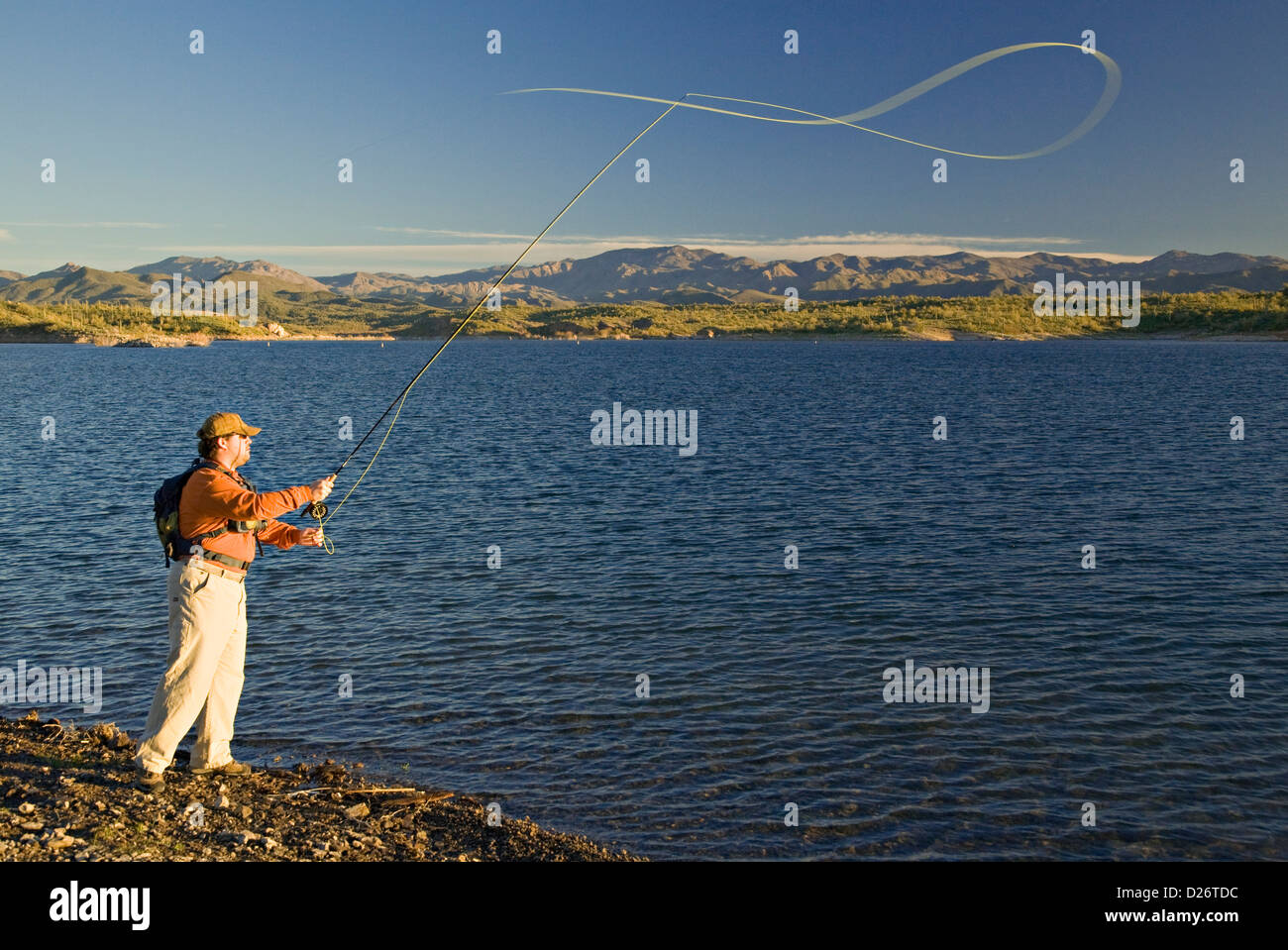 Man fly fishing along the desert shoreline of Lake Pleasant with the foothills of the Bradshaw Mountains in the distance. Stock Photo