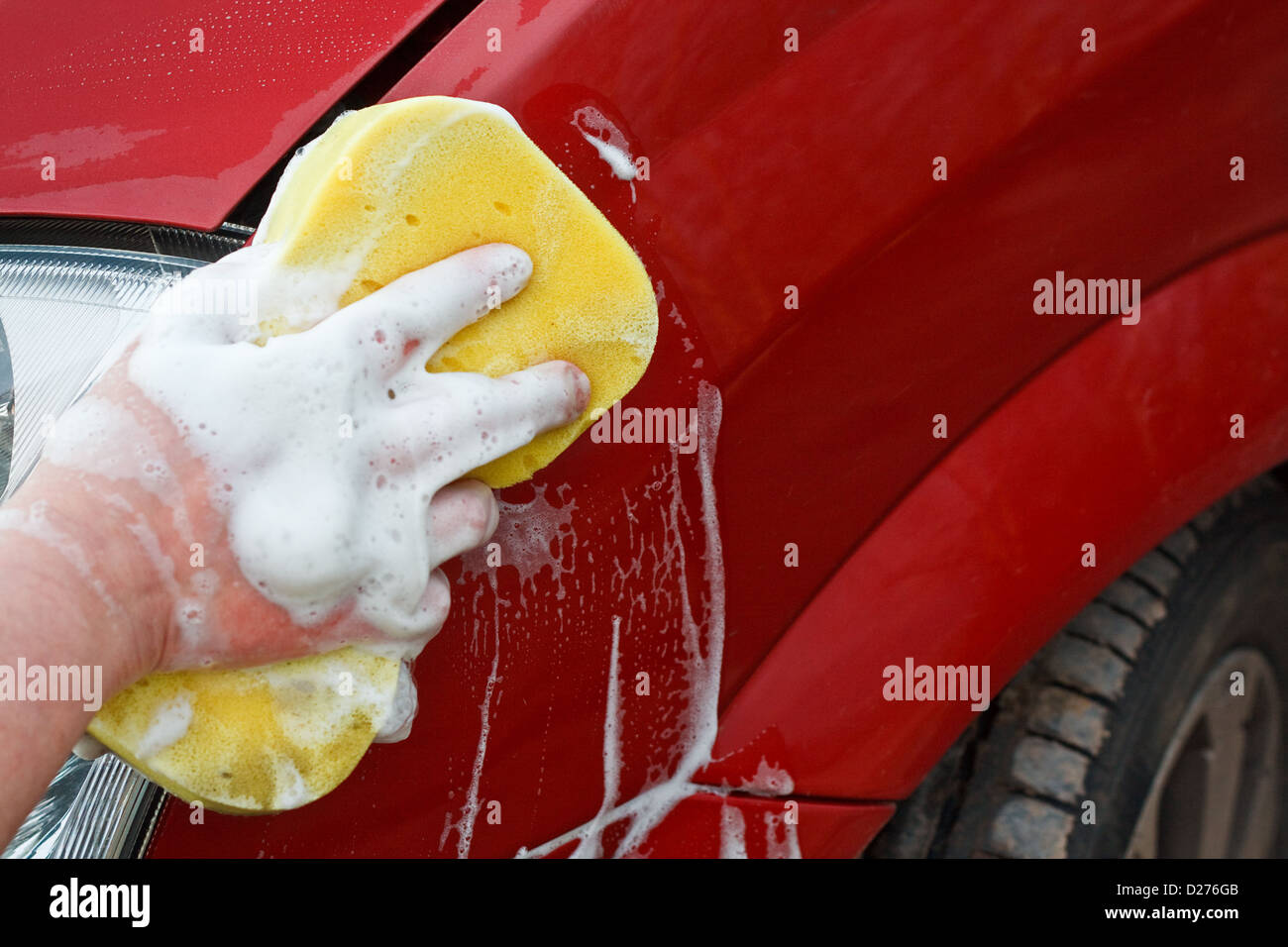 Washing the front wing of a car by hand with a yellow soapy sponge Stock Photo