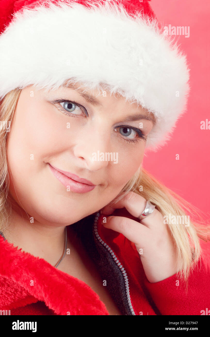 Portrait of joyful pretty woman in red santa claus hat smiling on red ...