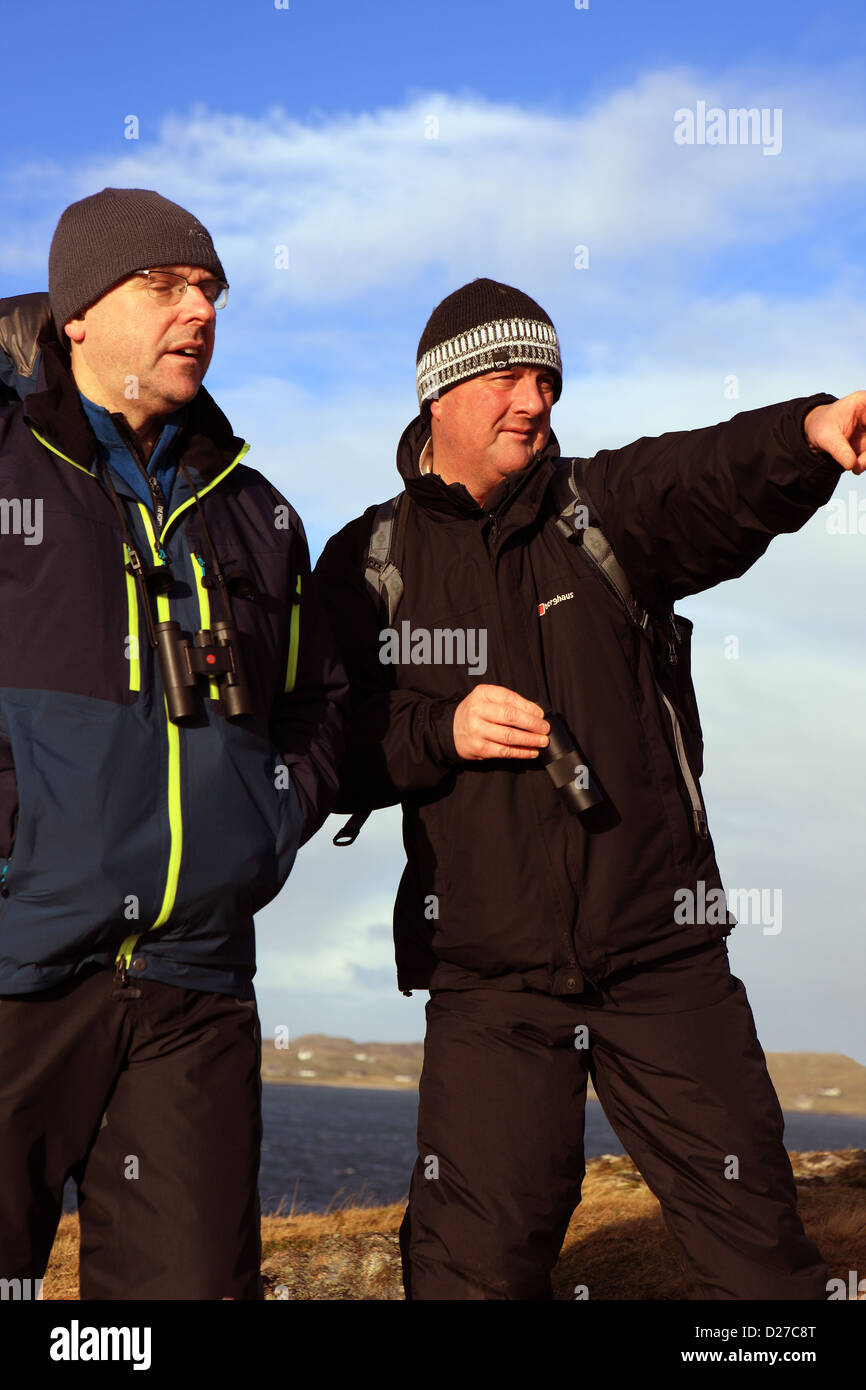 Two men with binoculars and monocular. One pointing at wildlife and both dressed in outdoor clothing Stock Photo