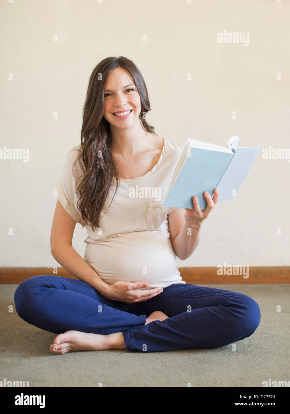 USA, Utah, Salt Lake City, Pregnant mid adult woman sitting with crossed legs and holding book Stock Photo