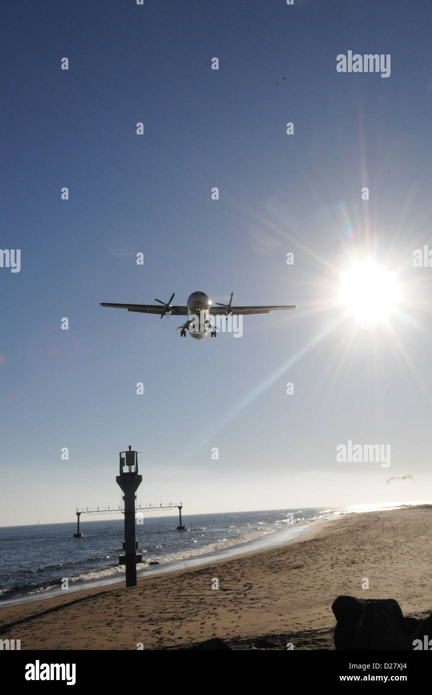 Propeller aircraft coming into land over beach with sun and blue sky in background Stock Photo