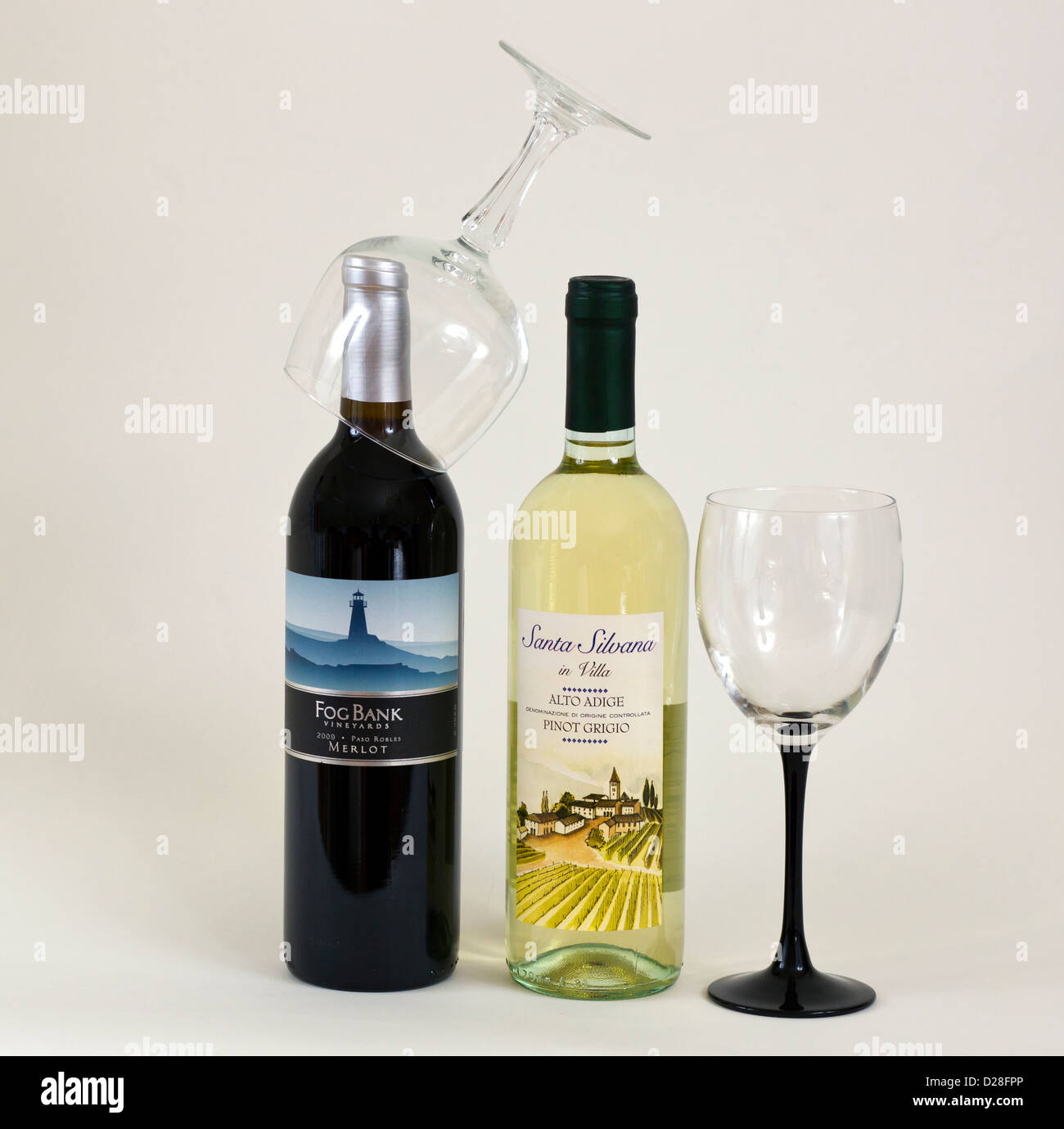 Two bottles of wine one white one red and two glasses. One glasses in upside down on the neck of the red wine. Stock Photo