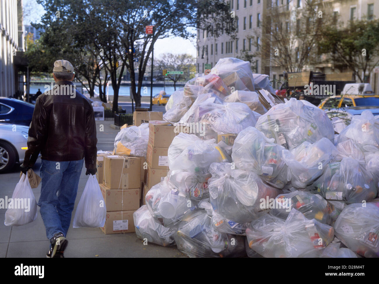 https://c8.alamy.com/comp/D28M4T/man-carrying-shopping-bags-passing-piles-of-plastic-garbage-bags-at-D28M4T.jpg