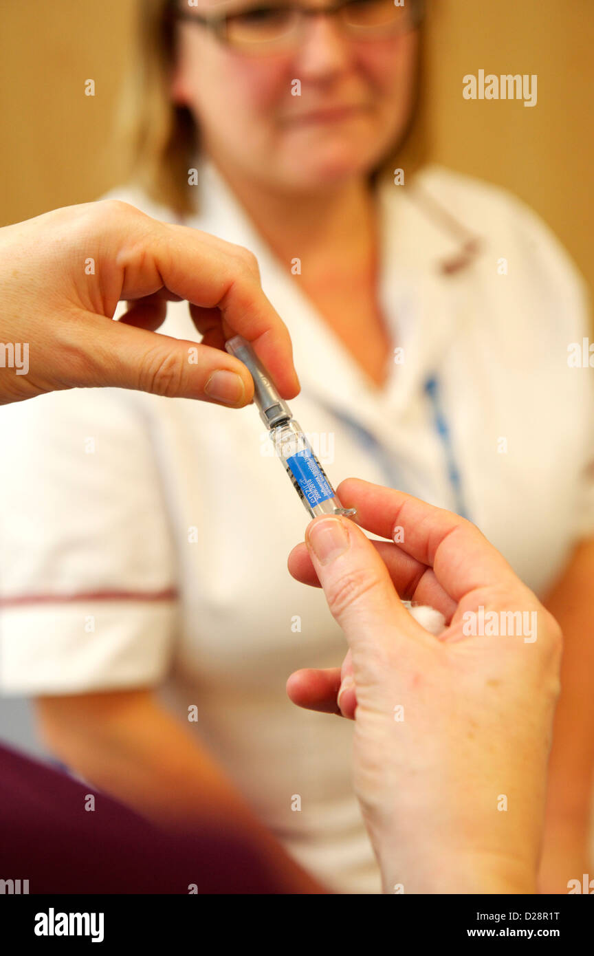 Nurse holding flu vaccine with NHS staff blurred in background before administering seasonal flu vaccine to frontline NHS staff Stock Photo