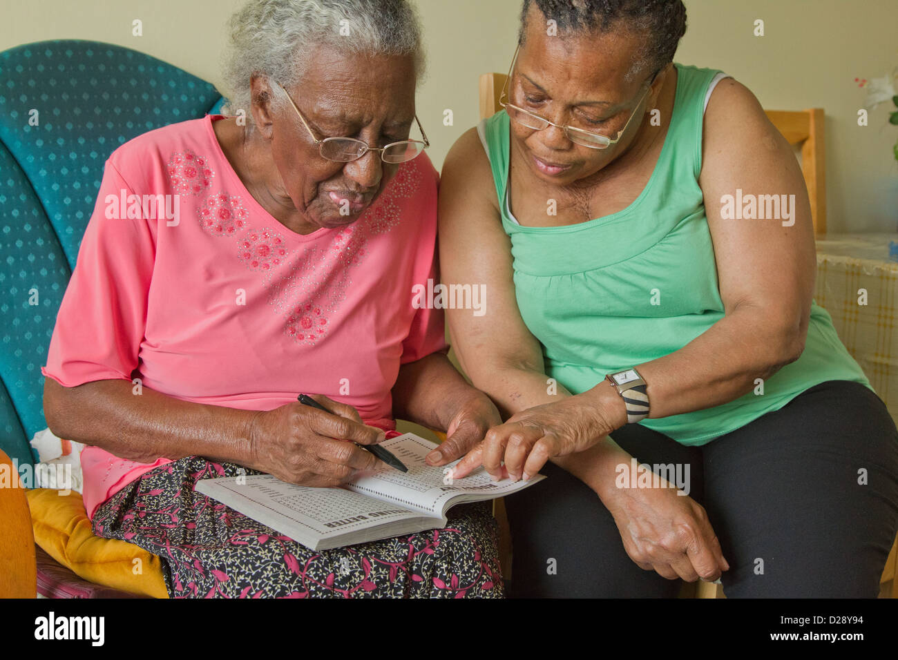 Carer and elderly visually impaired woman solving crossword. Stock Photo