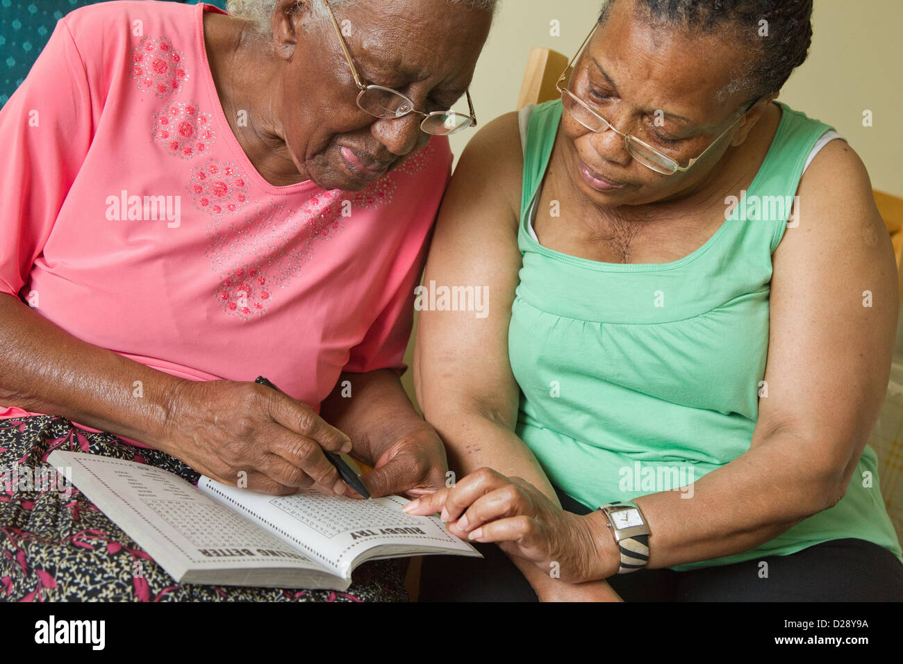 Carer and elderly visually impaired woman solving crossword. Stock Photo