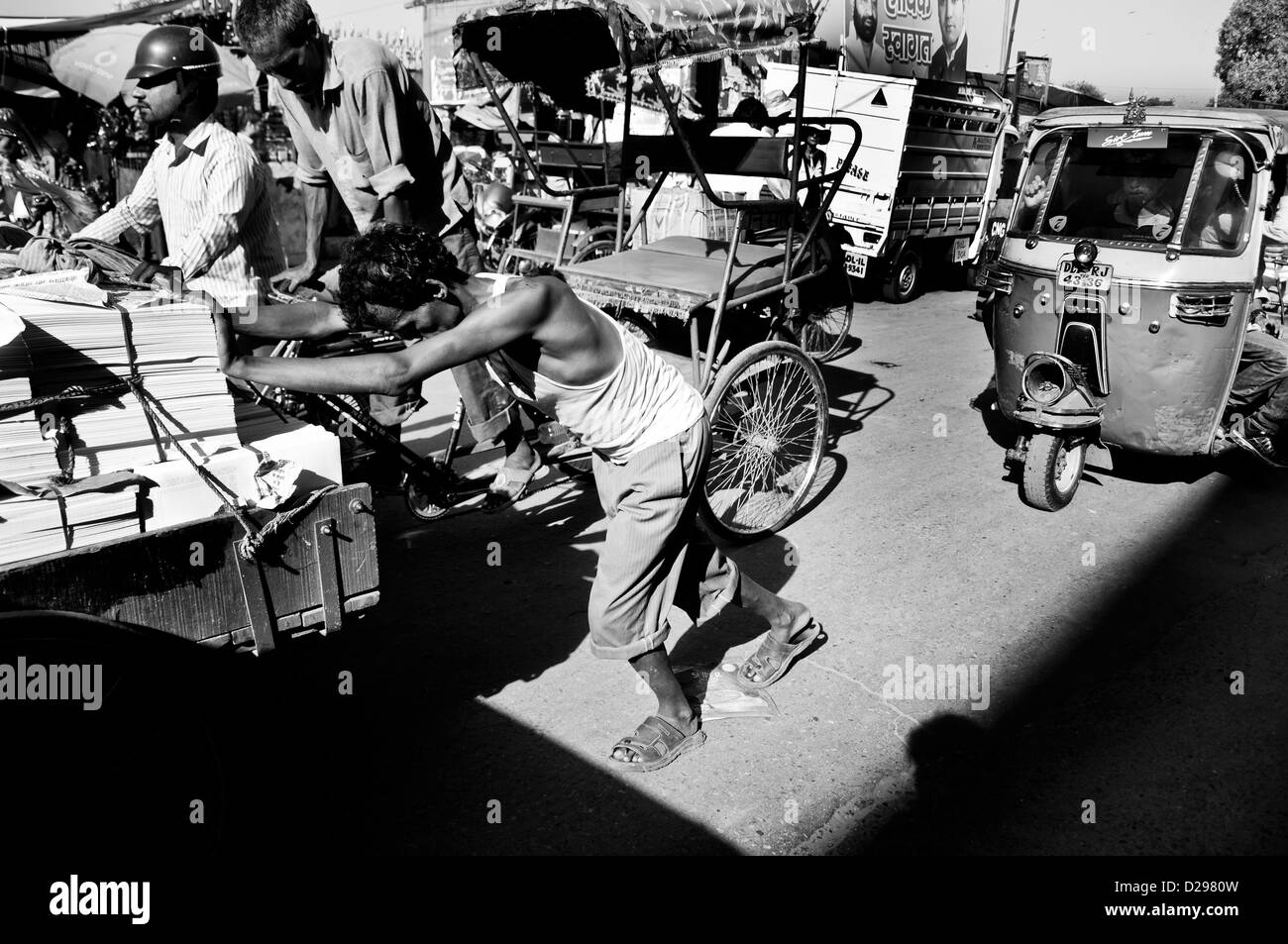 An old worker pushing a traditional loading cart containing books through the busy street of New Delhi. Stock Photo