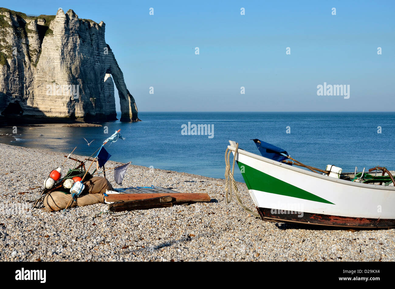 Small fishing boat on the famous pebble beach and cliffs of Etretat ...
