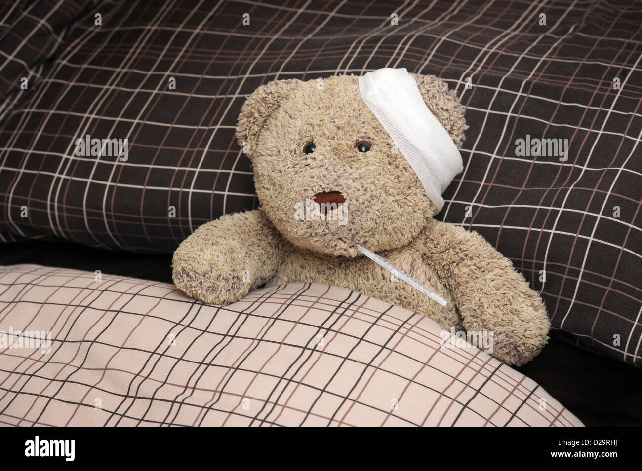 TEDDY BEAR IN BED WITH BANDAGE AND THERMOMETER RE ILLNESS MAN FLU SICKNESS THROWING A SICKIE TIME OFF WORK WORKERS DAY WELL UK Stock Photo