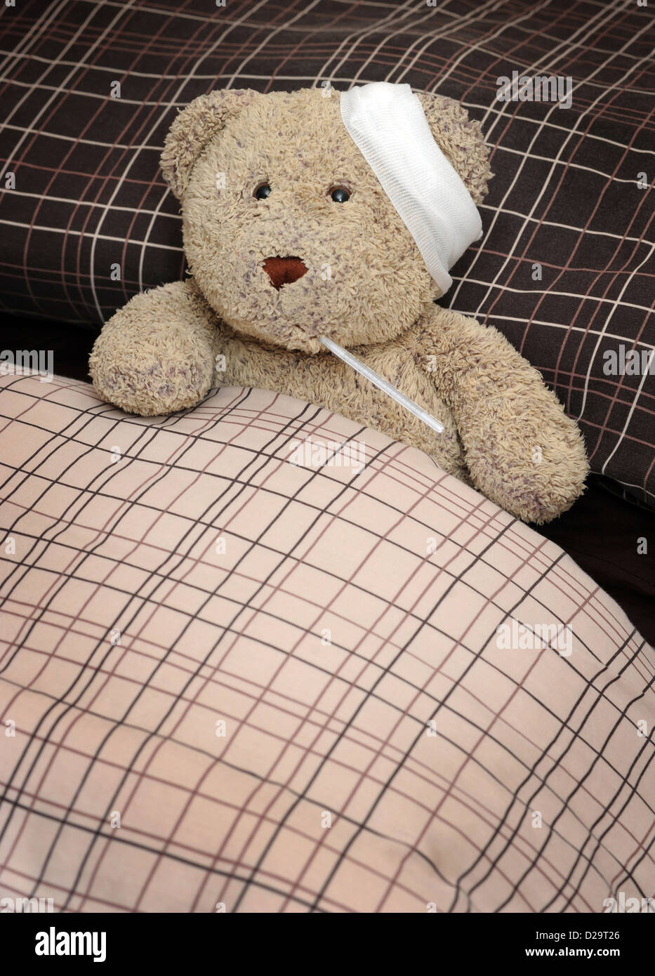 TEDDY BEAR IN BED WITH BANDAGE AND THERMOMETER RE ILLNESS MAN FLU SICKNESS THROWING A SICKIE TIME OFF WORK WORKERS DAY WELL UK Stock Photo