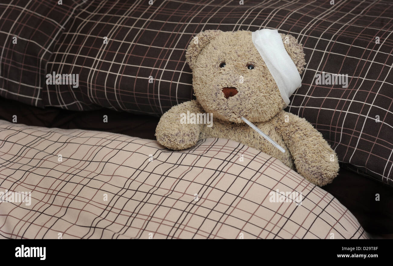 TEDDY BEAR IN BED WITH BANDAGE AND THERMOMETER RE ILLNESS MAN FLU SICKNESS THROWING A SICKIE TIME OFF WORK WORKERS DAY WELL UK Stock Photo