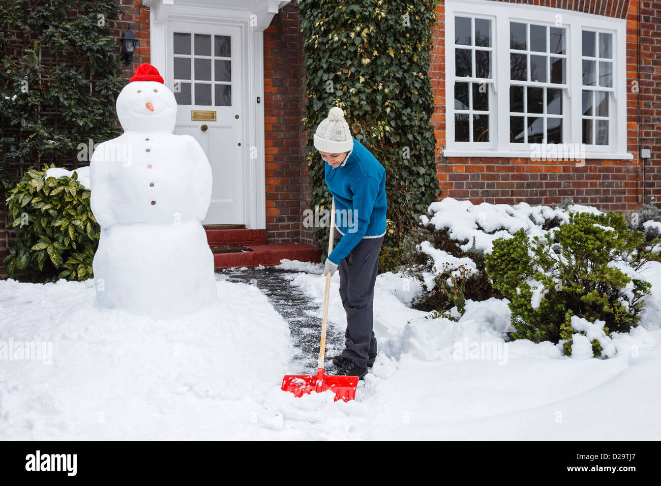 Woman shovels snow outside her home in UK Stock Photo