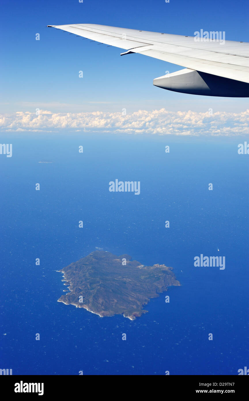 Airplane in flight over an islet in Mediterranean sea Stock Photo